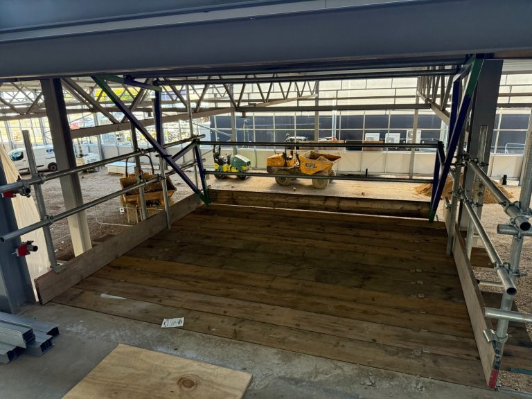 Empty construction site with scaffolding and wooden flooring, awaiting further work.