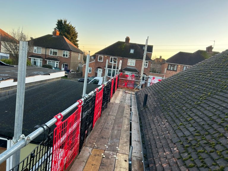 View of a rooftop walkway with safety barriers and residential houses in the background.