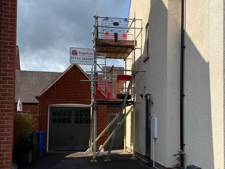 Scaffolding by a house with a construction sign and a garage in the background.