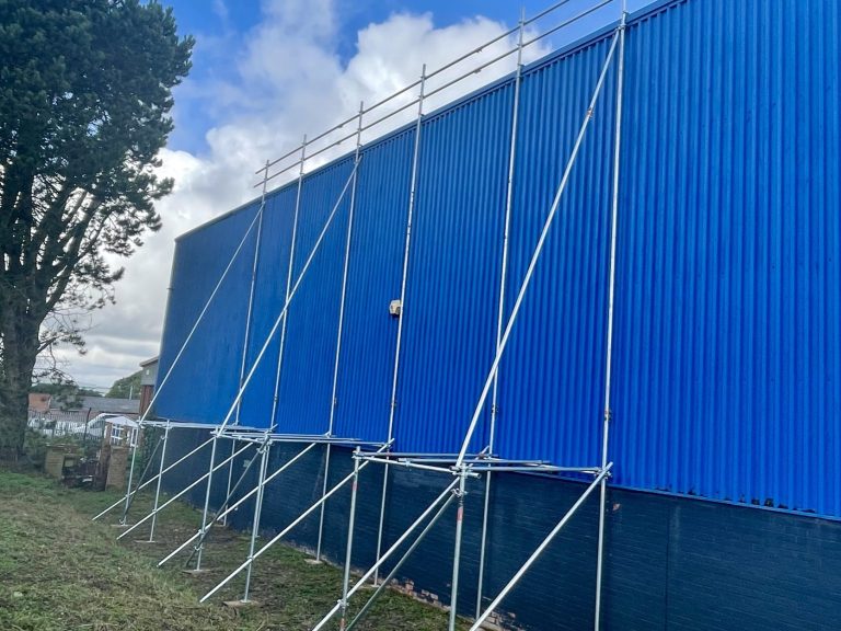 Scaffolding supports against a blue building with cloudy skies above.