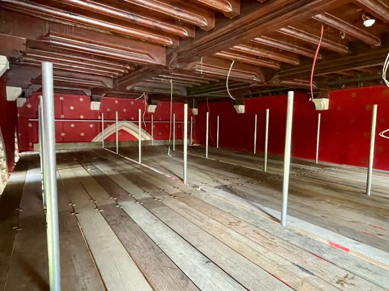 Interior of a spacious room with wooden beams, red walls, and vertical supports.