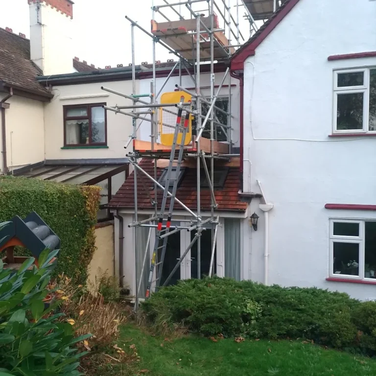 Scaffolding set up on a house, with a nearby garden and hedges visible.